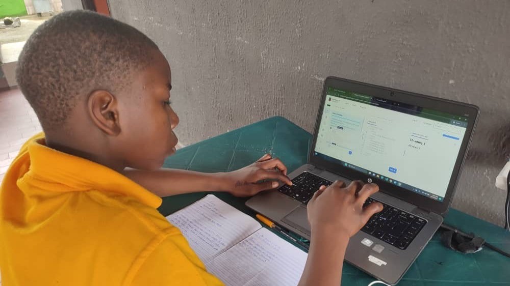 Young student in yellow hoodie focused on learning to code on laptop